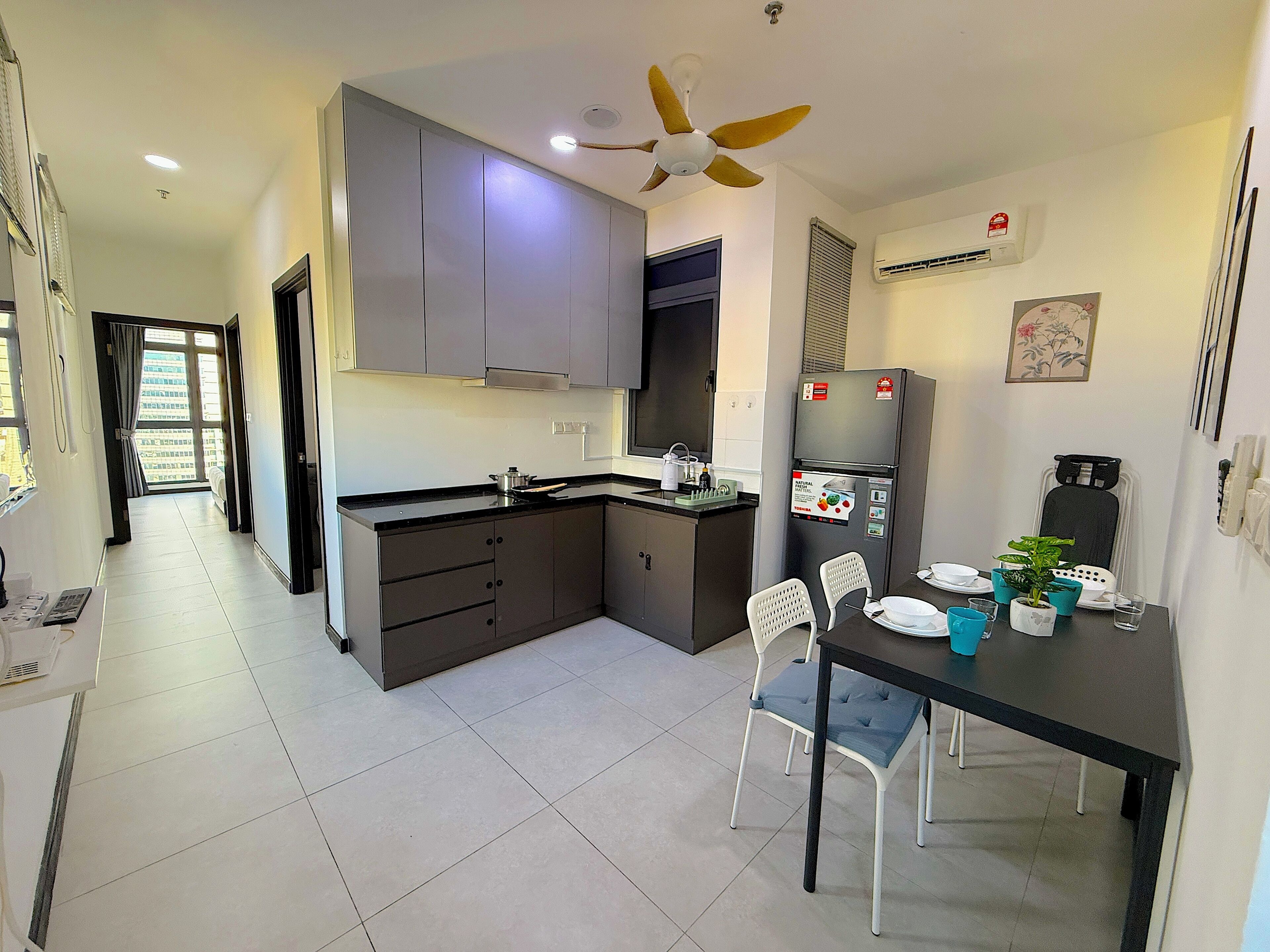 A modern kitchen with grey cabinets, a black countertop, and a built-in oven. There is a dining table with chairs and a small potted plant.