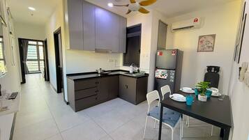 A modern kitchen with grey cabinets, a black countertop, and a built-in oven. There is a dining table with chairs and a small potted plant.