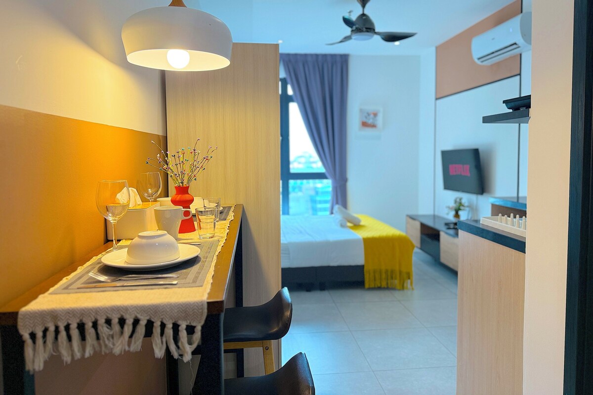 A hotel room with a dining area, a bed with a yellow bedspread, a ceiling fan, an air conditioning unit, and a television on the wall.