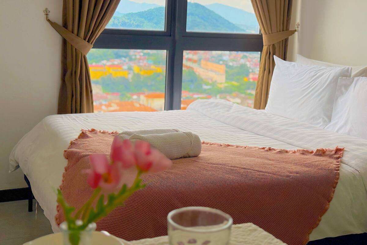 A bed with a view of a mountainous landscape through a window with curtains.
