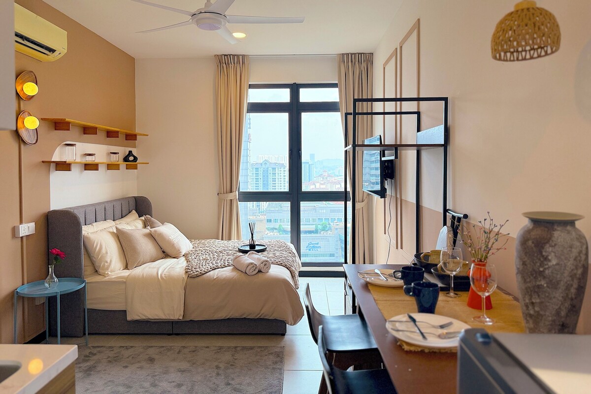 A modern hotel room with a bed, bedside table, and a dining area with a table and chairs.