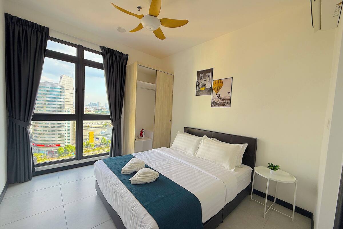 A modern hotel room with a large bed, a small bedside table, a ceiling fan, and a window with curtains.