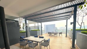 A covered outdoor patio with a wooden table and chairs, a pergola, and a view of the cityscape. - Neu Suites By Serenity Vacation Homes (Kuala Lumpur)