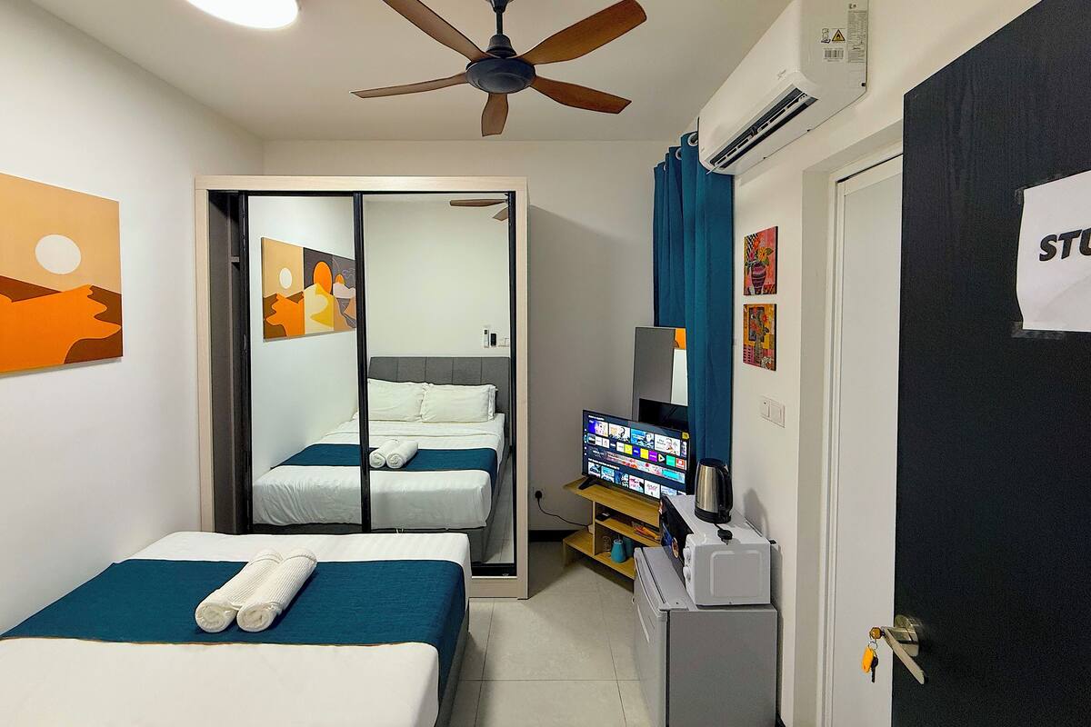 A hotel room with two beds, a ceiling fan, an air conditioning unit, a television, and artwork on the walls.