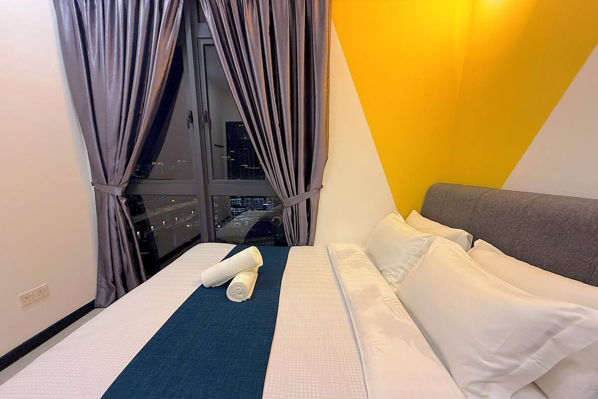 A hotel room with a bed, pillows, a blanket, and curtains.