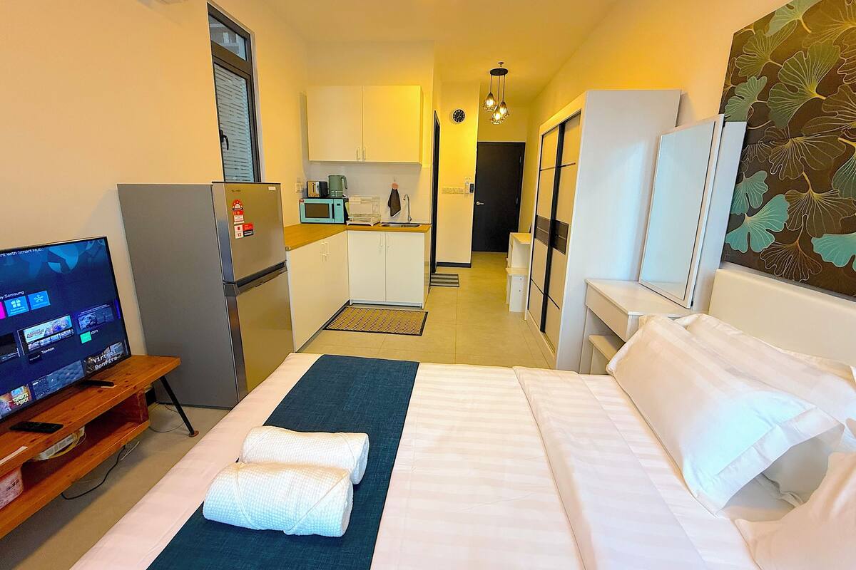 A hotel room with a bed, a desk, a television, a refrigerator, a microwave, and a sink.