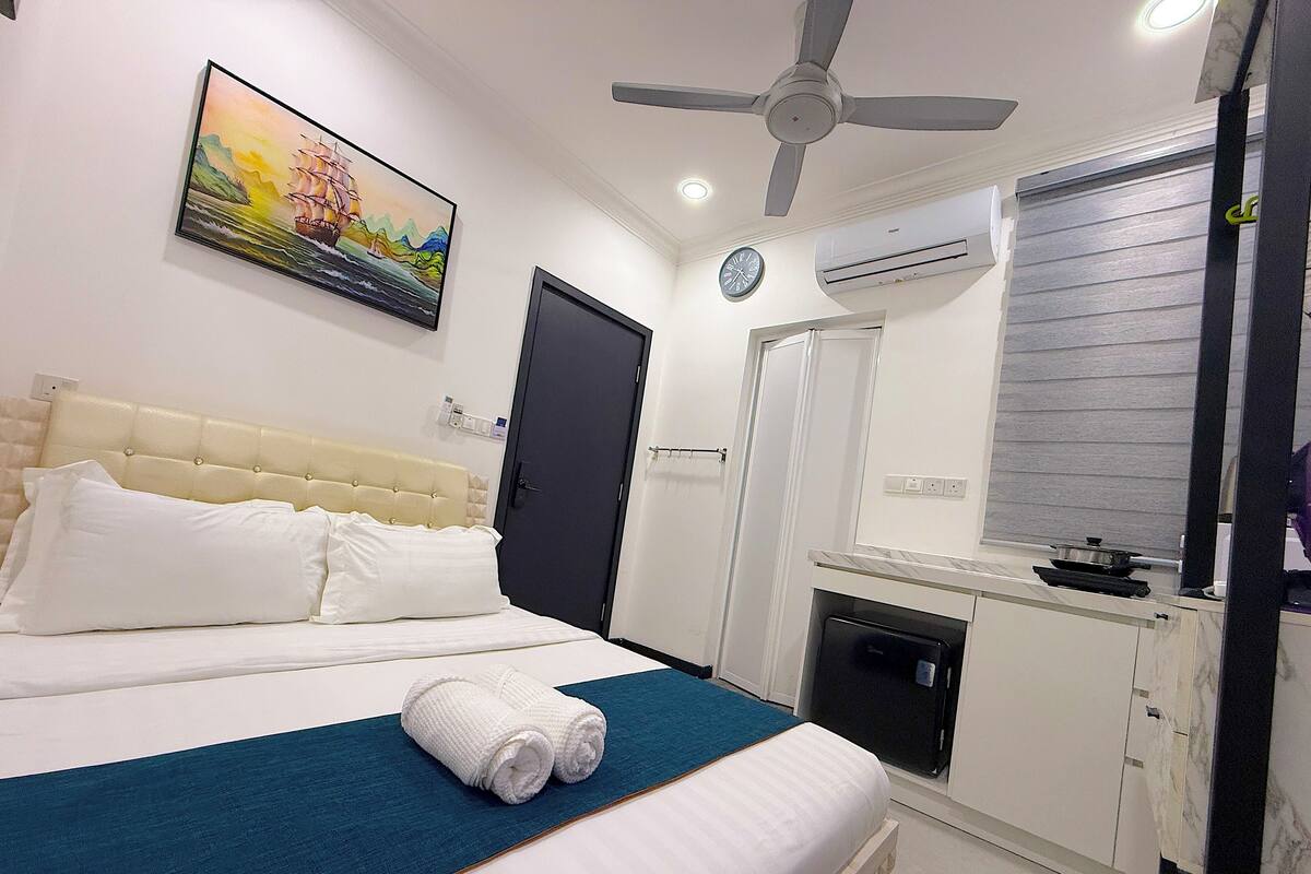 A hotel room with a bed, a ceiling fan, a painting, a clock, and an air conditioning unit.