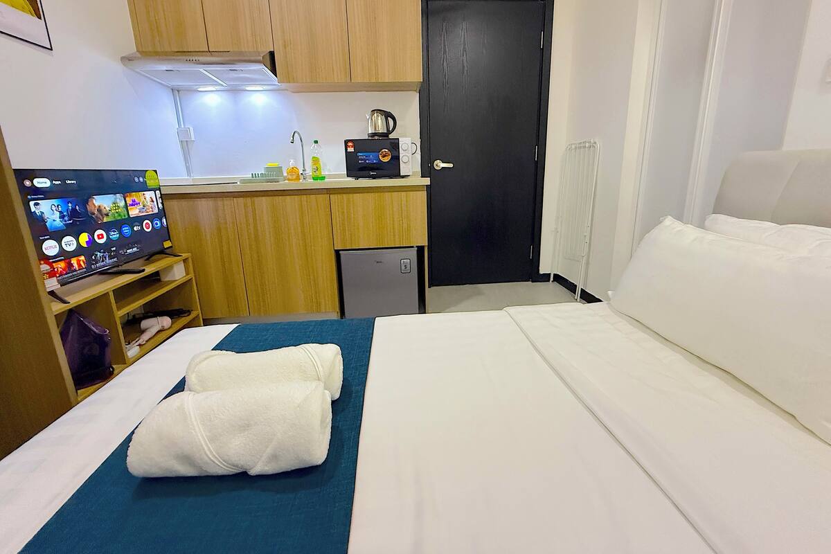 A hotel room with a bed, a TV on a stand, a small kitchenette, and a door.