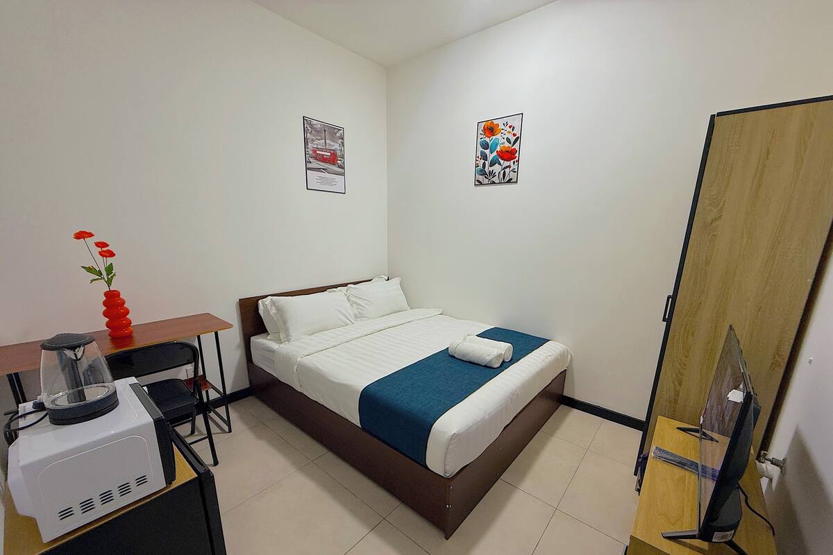 A hotel room with a bed, a desk, a coffee maker, a TV, and two framed pictures on the wall.