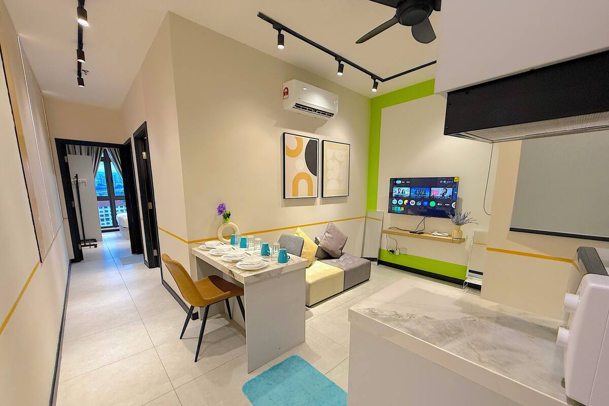 A modern hotel room with a dining area, a sofa, a TV, and an air conditioning unit.