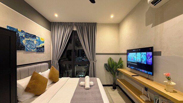 A modern hotel room with a bed, a TV, a plant, and a city view. - Neu Suites By Serenity Vacation Homes (Kuala Lumpur)