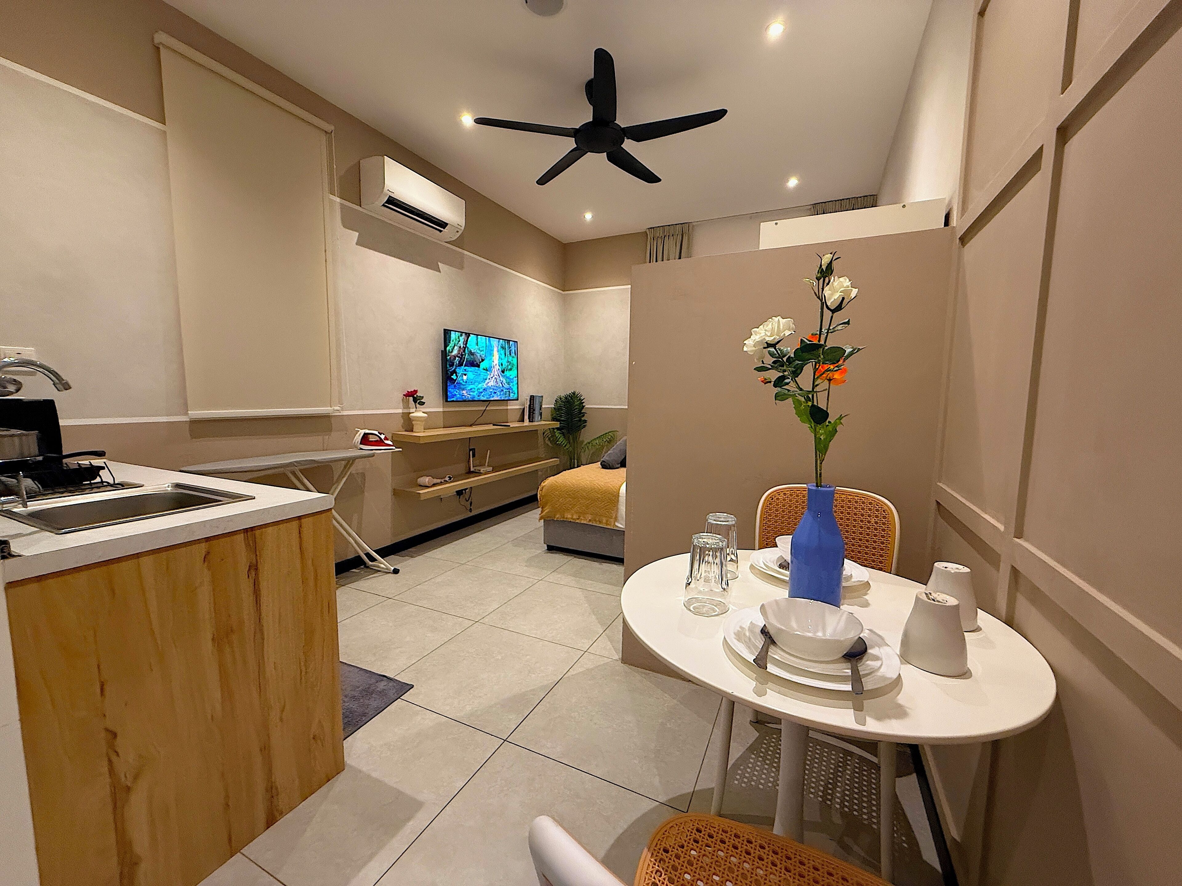 A compact living space with a kitchenette, a dining area with a table and chairs, a ceiling fan, and a TV mounted on the wall.