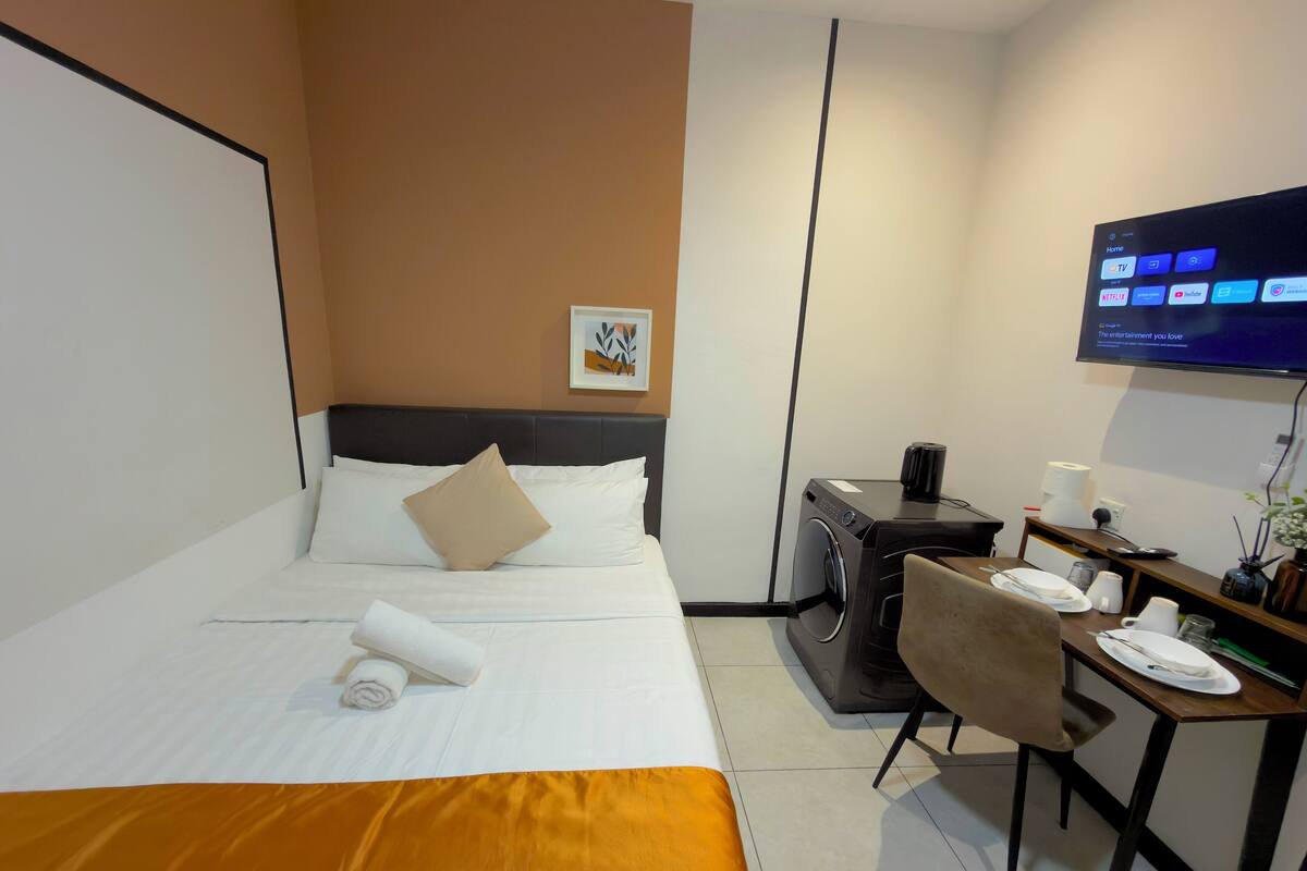 A hotel room with a bed, a desk, a washing machine, and a TV.