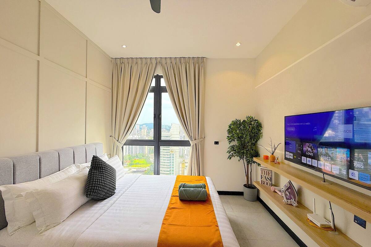 A hotel room with a bed, a TV, a plant, and a view of the city.