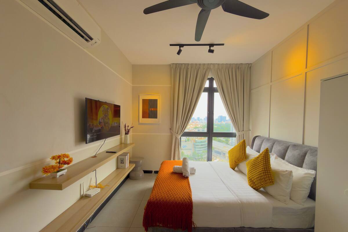 A modern hotel room with a bed, a TV, a desk, and a window with a city view.