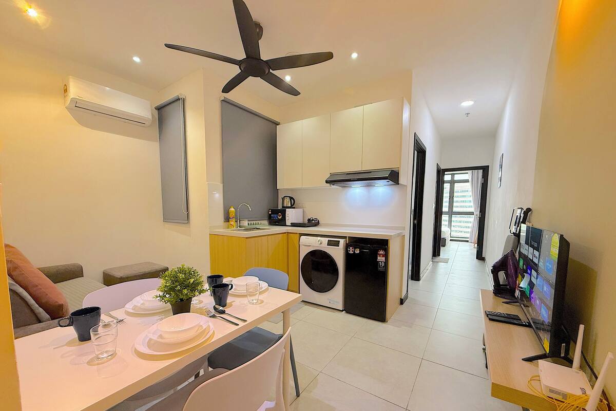 A compact living space with a dining area, kitchenette, washing machine, and a TV setup.