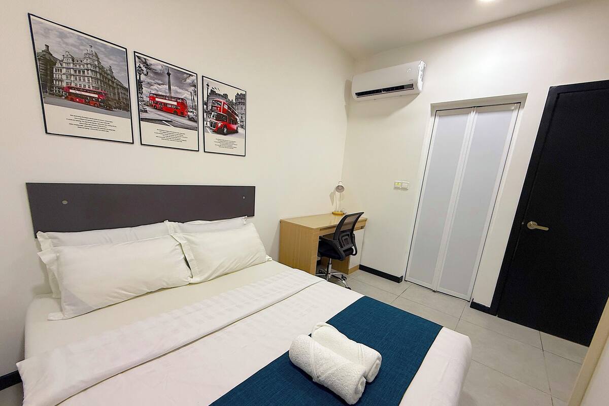A hotel room with a bed, a desk, a chair, an air conditioning unit, and a door.
