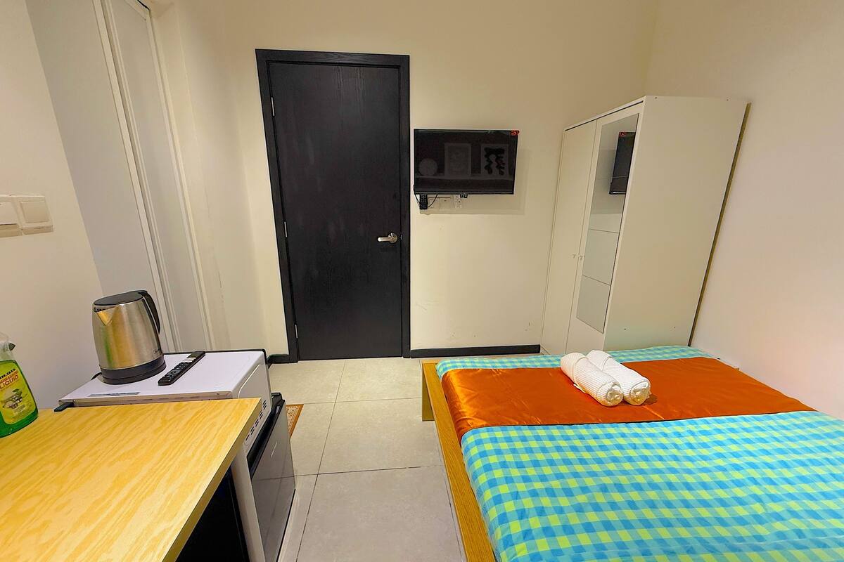 A hotel room with a bed, a desk with a kettle, a television, and a wardrobe.