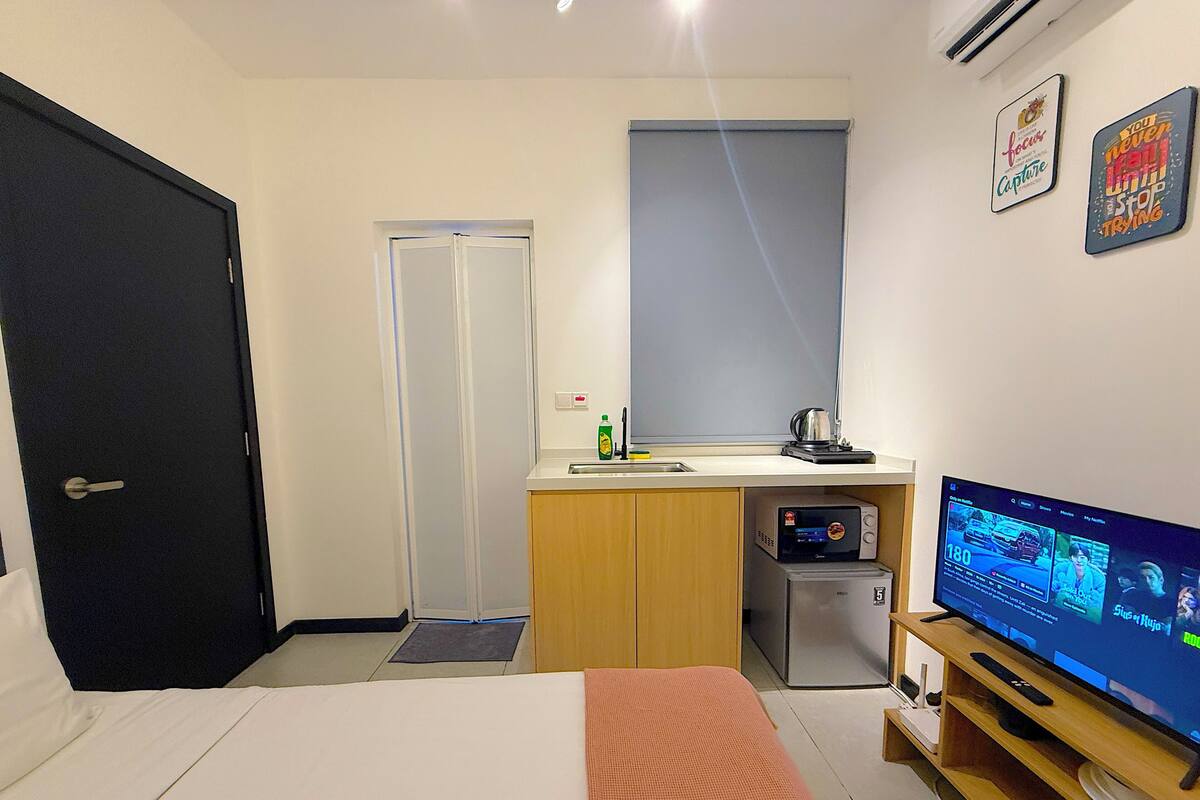A hotel room with a bed, a small kitchenette, a television, and a door.