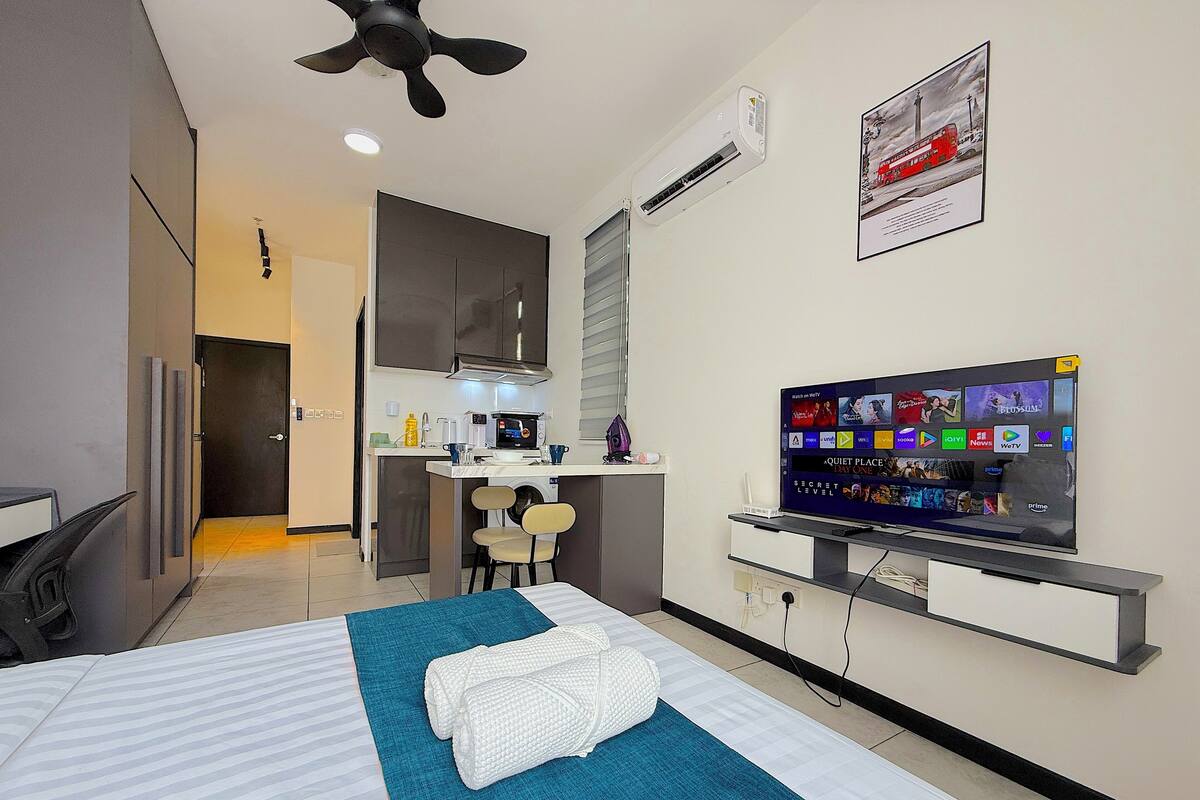 A modern hotel room with a bed, a TV, a small kitchenette, and a bathroom.