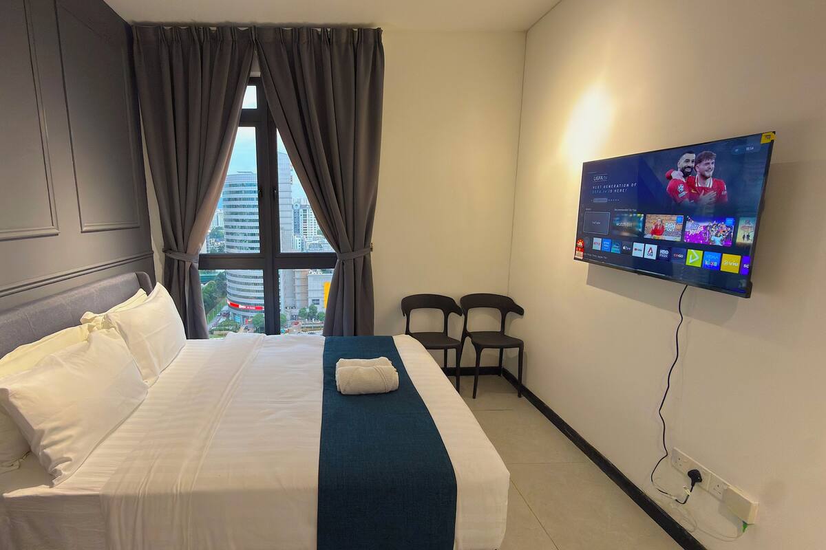 A hotel room with a bed, a TV mounted on the wall, and a window with curtains.