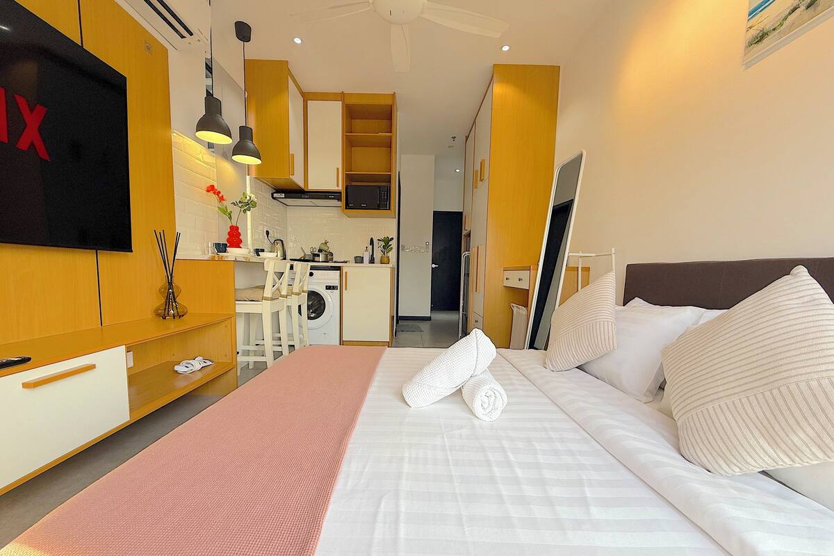 A hotel room with a bed, a TV, a kitchenette, and a bathroom.