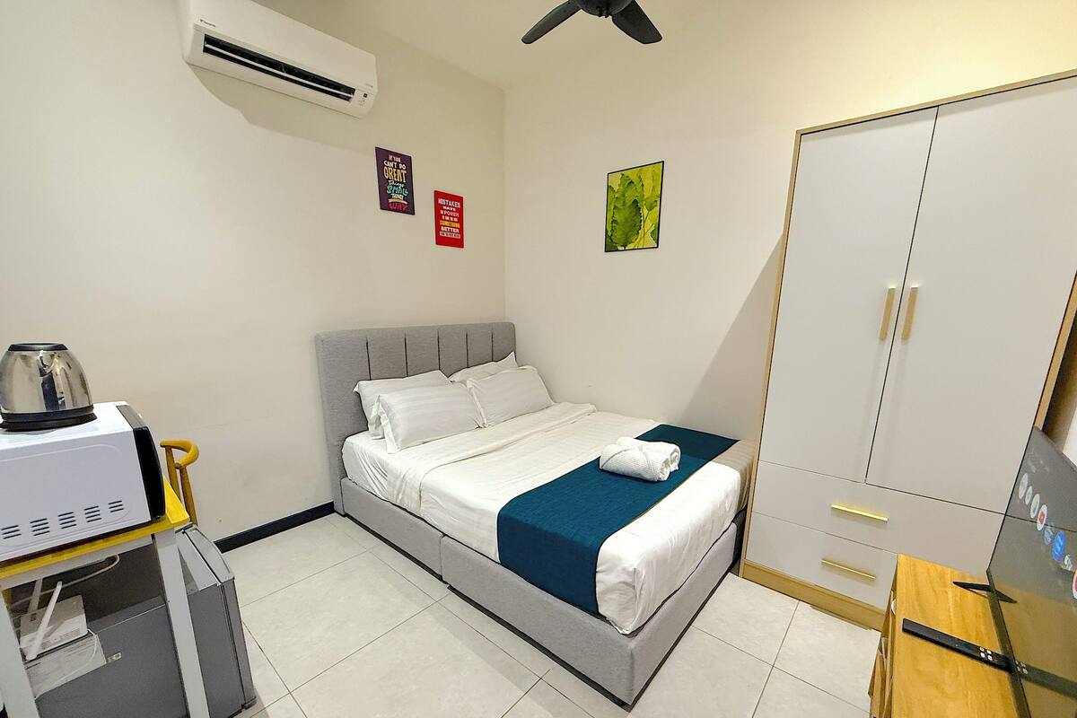 A hotel room with a bed, a wardrobe, a desk with a computer, and an air conditioning unit.