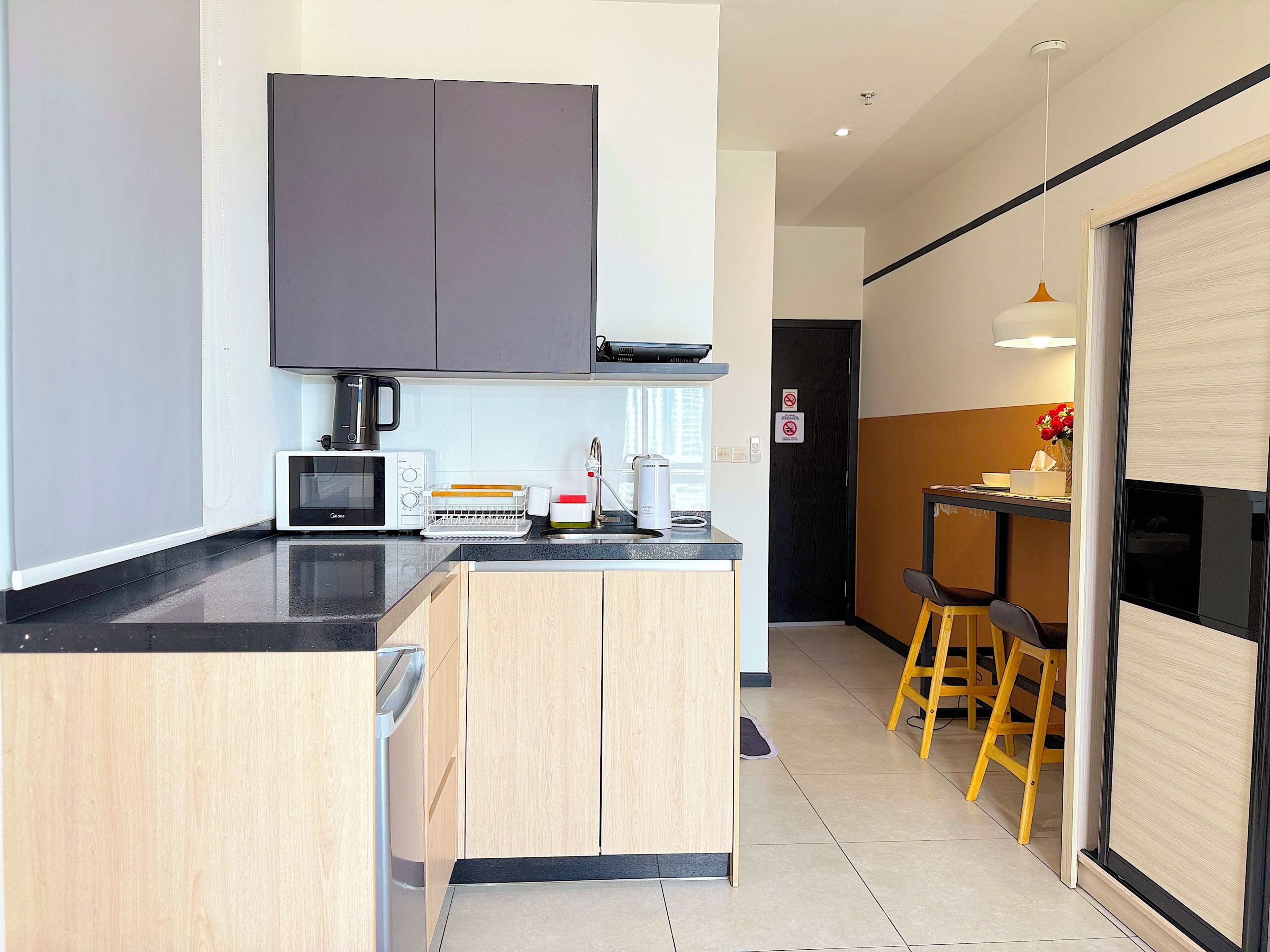 Eine moderne Küche mit Mikrowelle, Toaster und Kaffeemaschine auf der Arbeitsfläche. Darunter befindet sich ein Holzschrank und rechts ein Fenster mit schwarzem Rahmen.