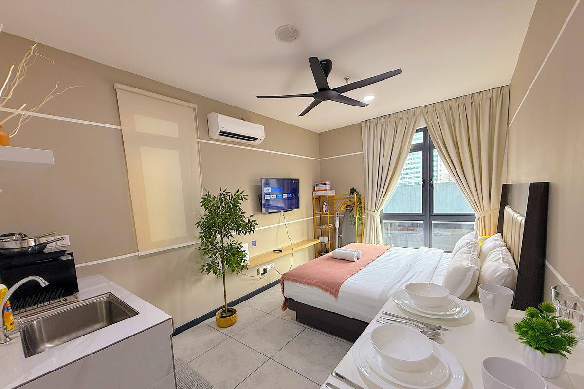A hotel room with a bed, a desk with dining set, a TV, an air conditioner, and a window with curtains.