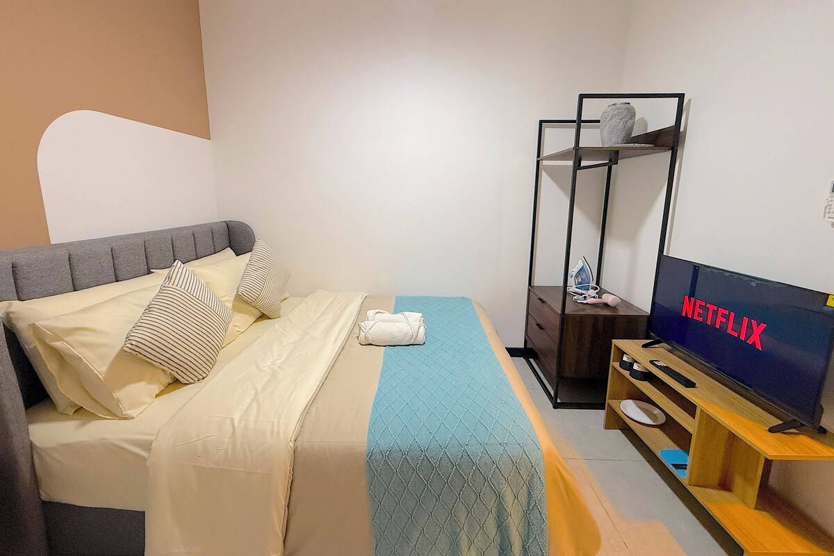 A bedroom with a bed, a TV, a wooden TV stand, and a metal shelf unit.