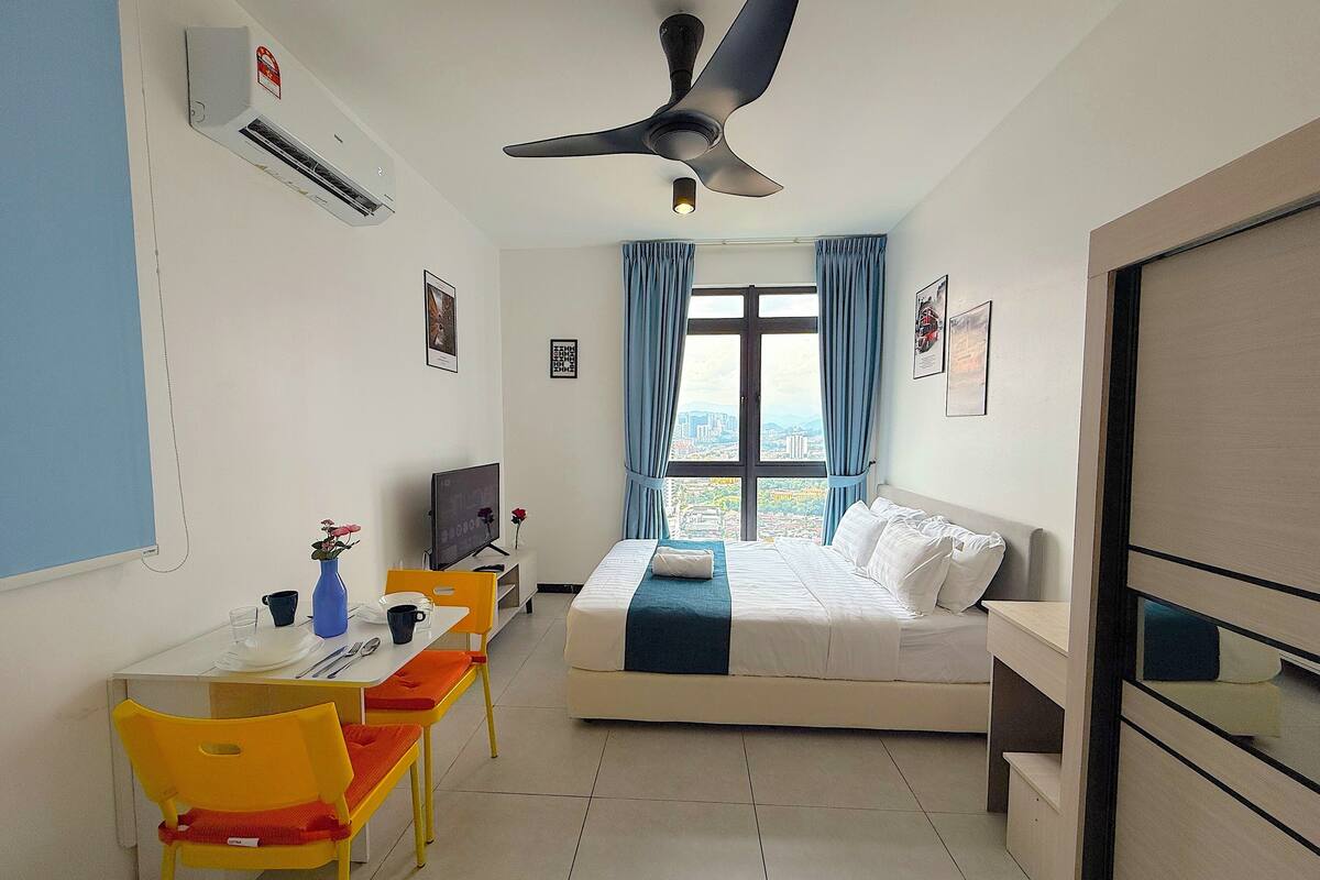 A hotel room with a bed, a desk with a chair, a TV, and a window with curtains.