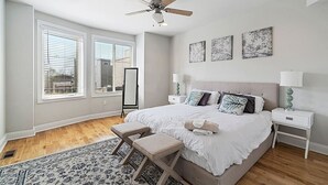 Un dormitorio con una cama grande, dos mesitas de noche, un ventilador de techo y una ventana con persianas.
