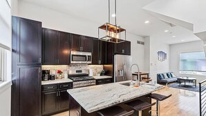 Una cocina moderna con armarios oscuros, electrodomésticos de acero inoxidable, una isla con encimera de mármol y un taburete de bar.