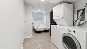 Un cuarto de lavandería con lavadora, secadora y una cama en la habitación contigua.