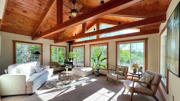 Ein geräumiges Wohnzimmer mit hohen Decken, großen Fenstern und Holzbalken.