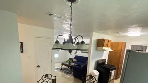 A dining area with a glass table and metal chairs, a chandelier, and a kitchen in the background. - “Cozy Diamond on the Corner” (Port Arthur)