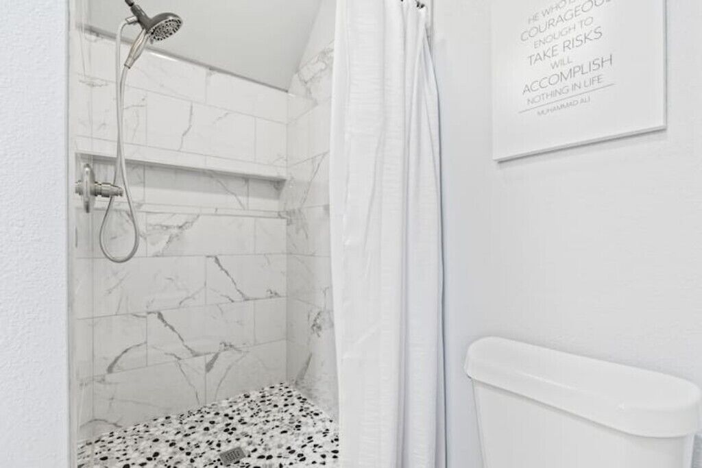 A bathroom with a shower, a toilet, and a marble-tiled wall.