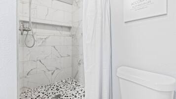 A bathroom with a shower, a toilet, and a marble-tiled wall.