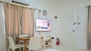 Ein Zimmer mit Esstisch, Stühlen, einem Fernseher, der eine Willkommensnachricht zeigt, einer Uhr und einem Feuerlöscher.