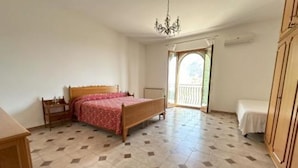 A bedroom with a bed, a wooden wardrobe, a small table, and a chair. - CHRIS Villa (Taormina)