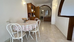 A dining area with a table set for four, surrounded by white chairs, and a wooden cabinet with various items. - CHRIS Villa (Taormina)