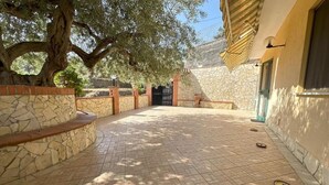 A courtyard with stone walls, a tree, and a building entrance. - CHRIS Villa (Taormina)