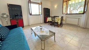 A living room with a sofa, a glass-top coffee table, a dining table with chairs, a TV, and a window with curtains. - CHRIS Villa (Taormina)