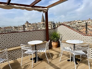 A terrace with two white tables and chairs, a potted plant, and a patterned wall.