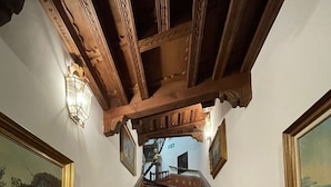 Uma escadaria com elegantes balaústres de madeira e azulejos estampados, que leva a um patamar com vista para outra escadaria e uma porta.