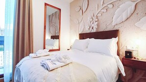 Una habitación de hotel con una cama grande, un espejo, una mesita de noche y una pared con motivos florales.