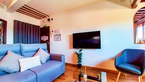 Una sala de estar con un sofá, una silla, un televisor de pantalla plana y una planta en maceta.