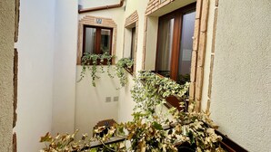 Un patio estrecho con una pared blanca, un banco de madera y una ventana con marco de ladrillo.