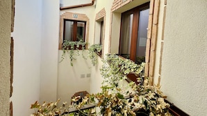 A narrow courtyard with a white wall, a wooden bench, and a window with a brick frame. - Casón De Los López Apartments 1B (Toledo)
