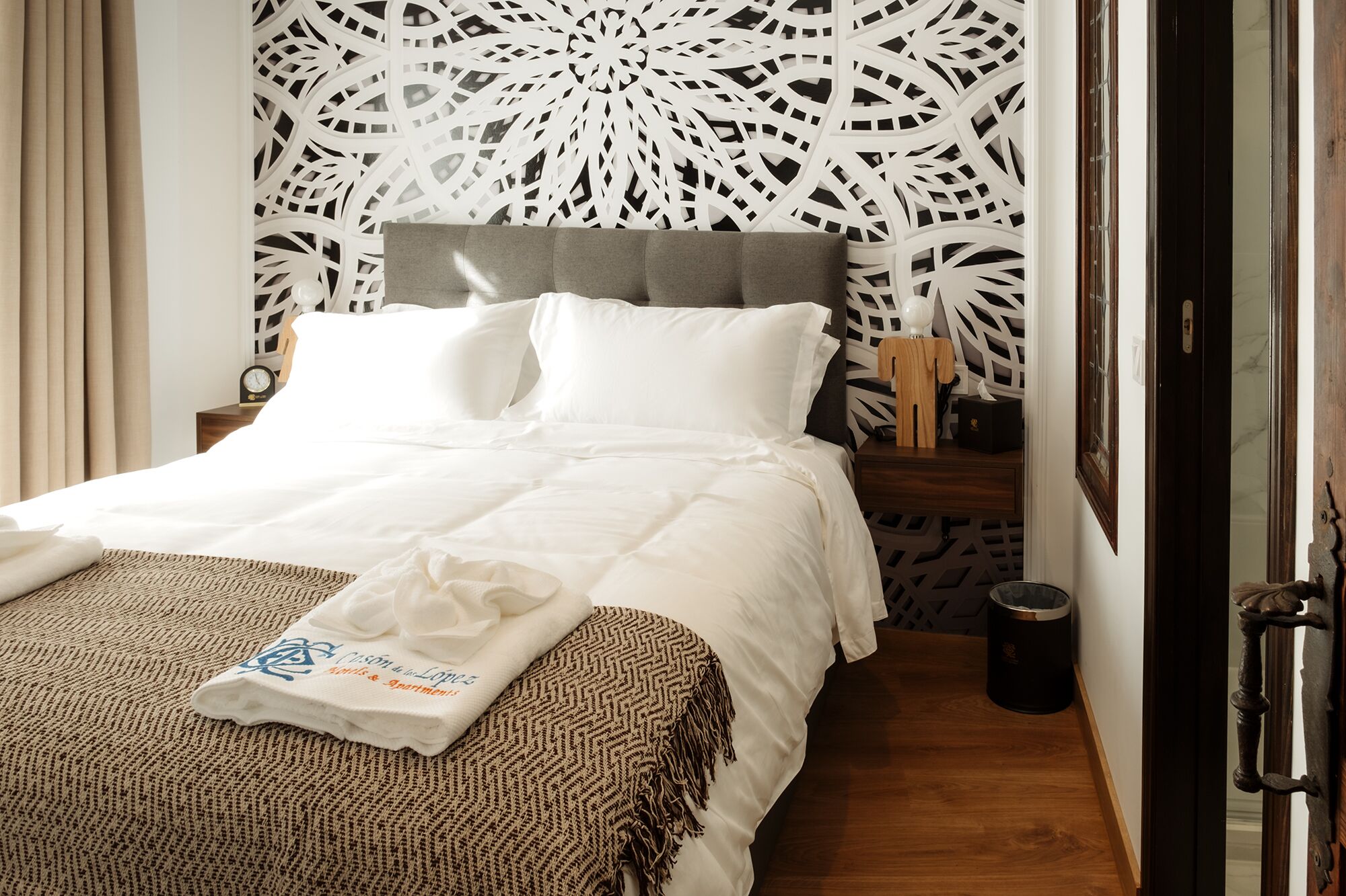Una cama bien hecha con sábanas blancas, un plaid y una toalla con texto.